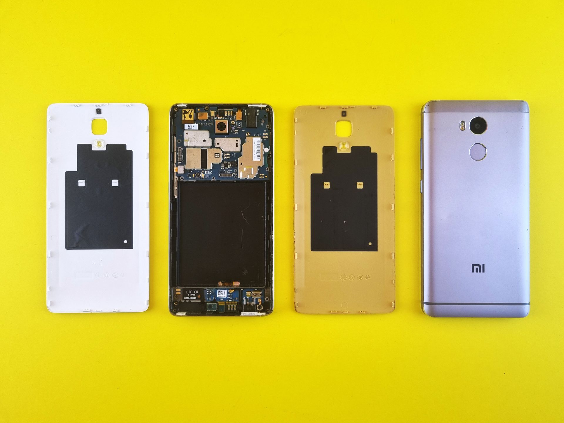 Close-up of disassembled smartphone on vibrant yellow surface, showing various parts.